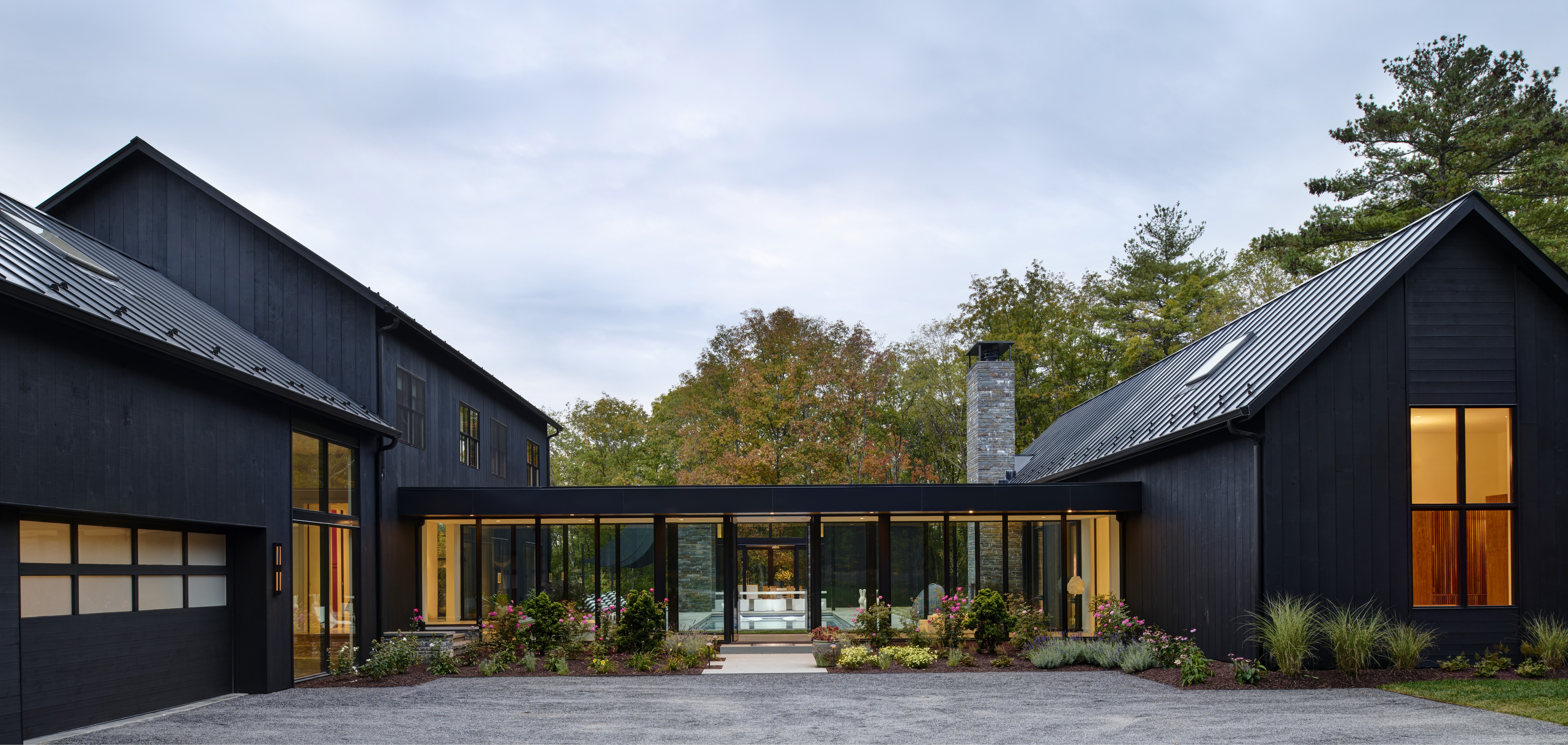 Exterior view of Wass House by Studio MM Architect, featuring two black gabled volumes connected by a central glass breezeway under a cloudy sky.