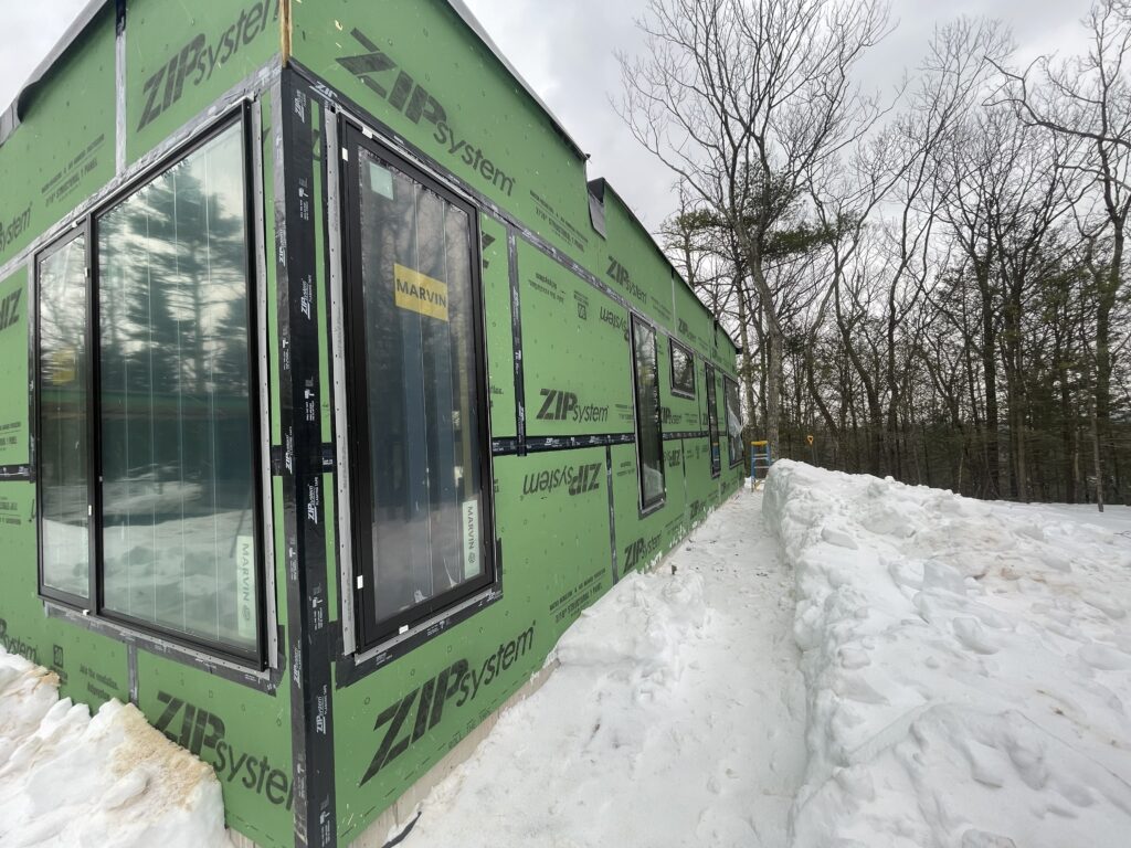 Exterior detail shot of the green ZIP System wall sheathing on Quattro. Multiple black-framed Marvin windows are installed and taped for weatherproofing. 