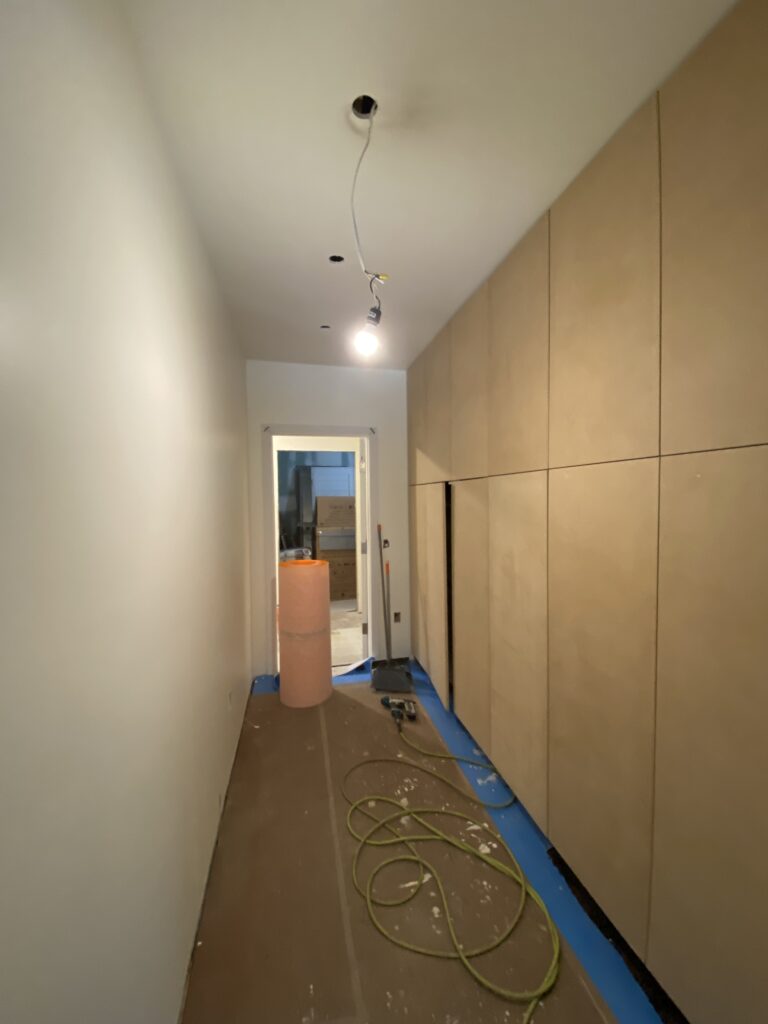A hallway perspective at Jardin66 highlighting a seamless wall of custom floor-to-ceiling wooden storage cabinets. The clean, handle-less design emphasizes the minimalist modern aesthetic of the renovation, with temporary construction lighting and floor protection still in place.