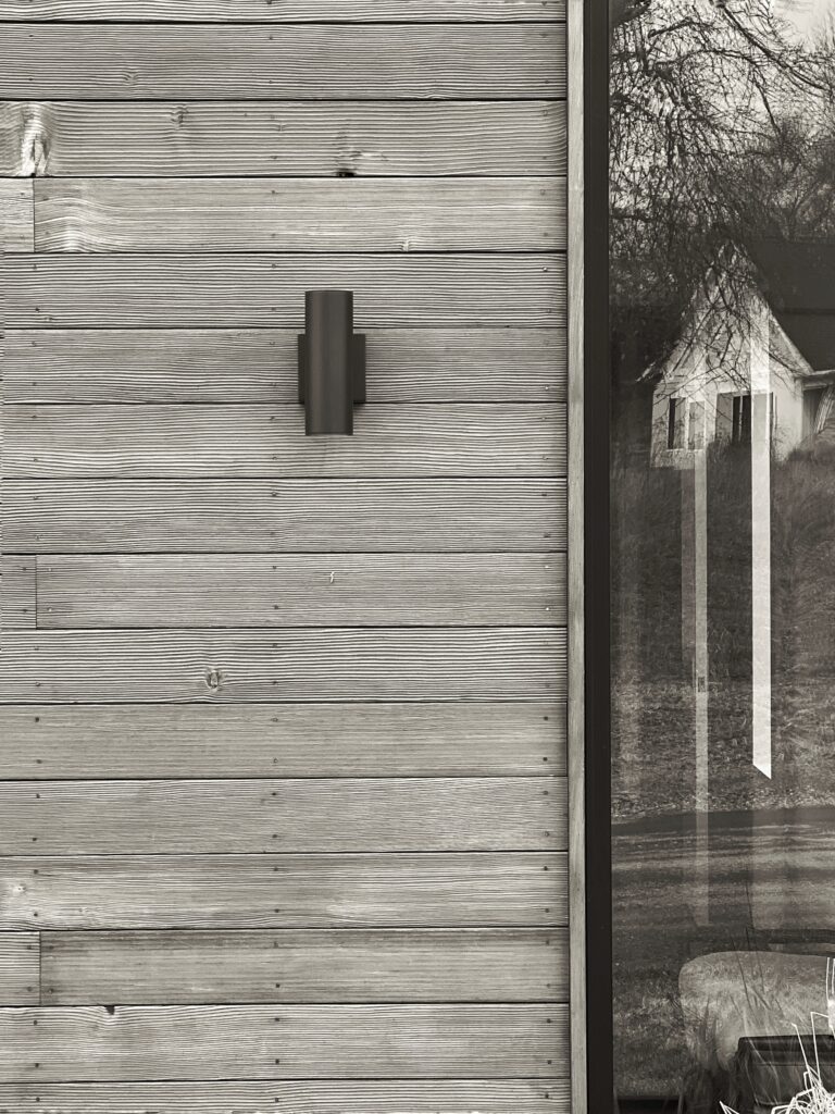 Detail of modern residential exterior at Barnstormer by Studio MM Architect, showing the contrast between natural wood texture and minimalist black lighting fixtures.