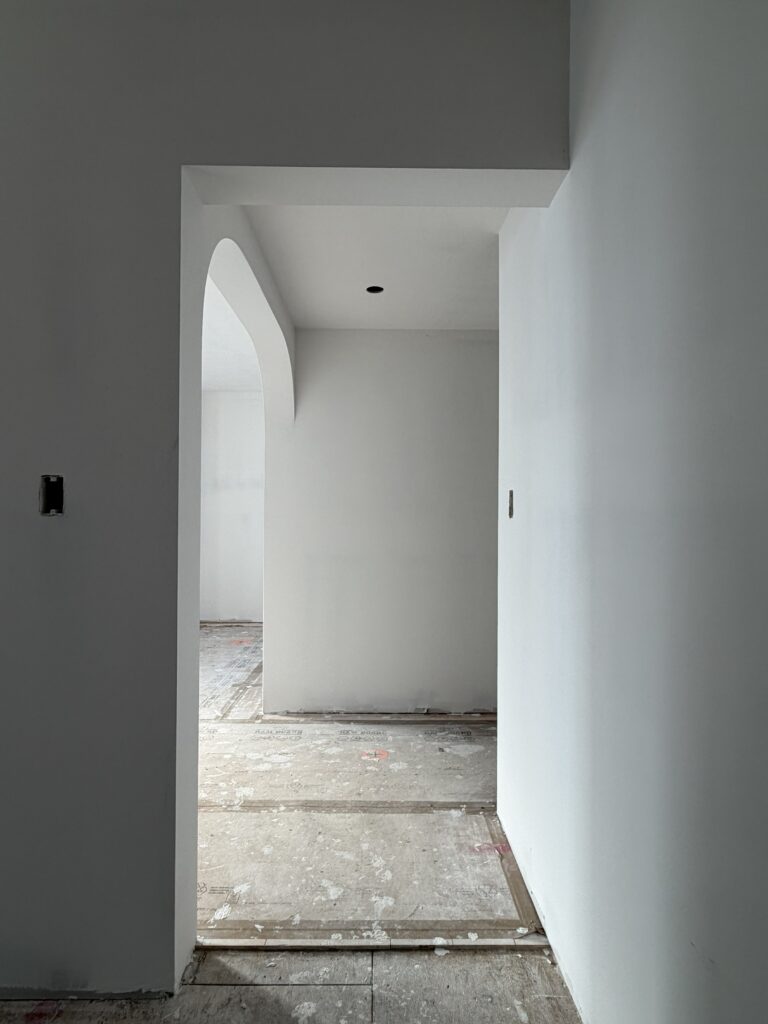 A perspective shot through a series of doorways at Hudson House. The view captures the minimalist aesthetic of the project, featuring sharp geometric lines contrasted by a rounded arched opening in the distance, emphasizing the depth and light of the new interior layout.