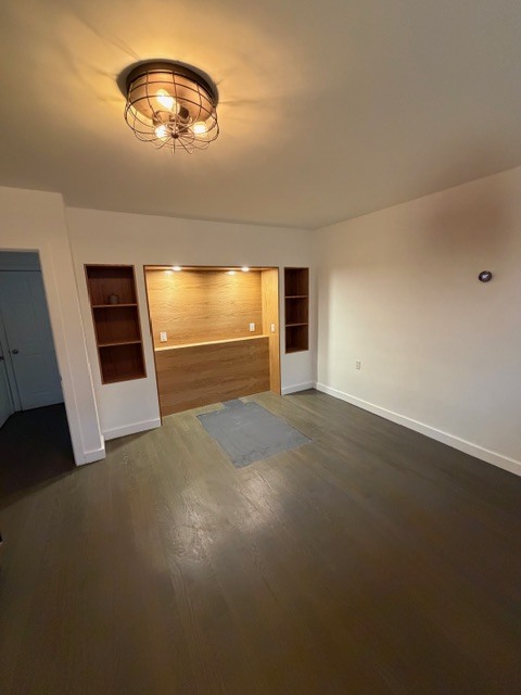 A renovated bedroom at Shokan Reno showing a custom wood-paneled headboard niche with integrated lighting and flanking open shelving. The room is finished with dark-stained wood floors and a vintage-style industrial wire cage ceiling light.
