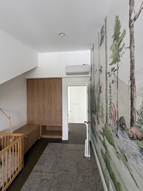 Interior view of a nursery at Shokan Reno, featuring custom light-wood built-in cabinetry and a low bench. The focal point is a detailed wall mural depicting a forest scene with woodland animals like deer and bears, illustrating a playful yet modern Hudson Valley interior.