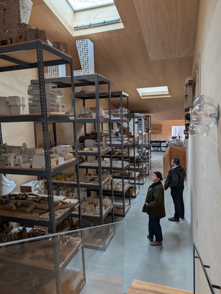Alexa and Holdt of Studio MM Architect touring the Steven Holl Architects Architectural Archive at T Space in Rhinebeck, NY, surrounded by floor-to-ceiling shelves of white architectural models.