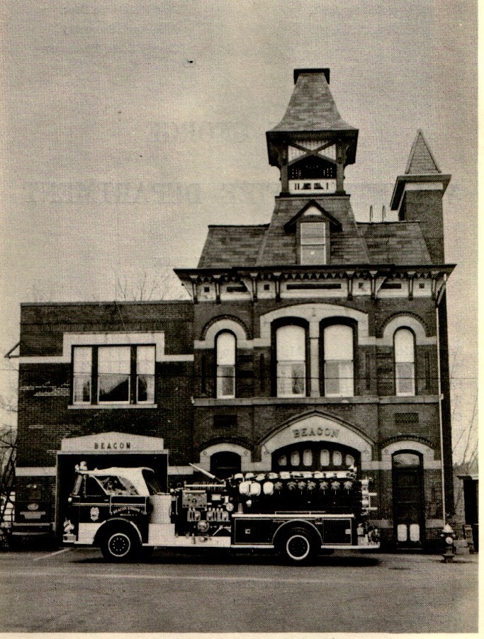 A historic black and white photo of the Beacon firehouse from the late 19th or early 20th century. A horse-drawn fire carriage is visible inside the central arched bay. The building features intricate brickwork, a mansard-style roof section, and a prominent wooden bell tower with an ornate pointed roof.