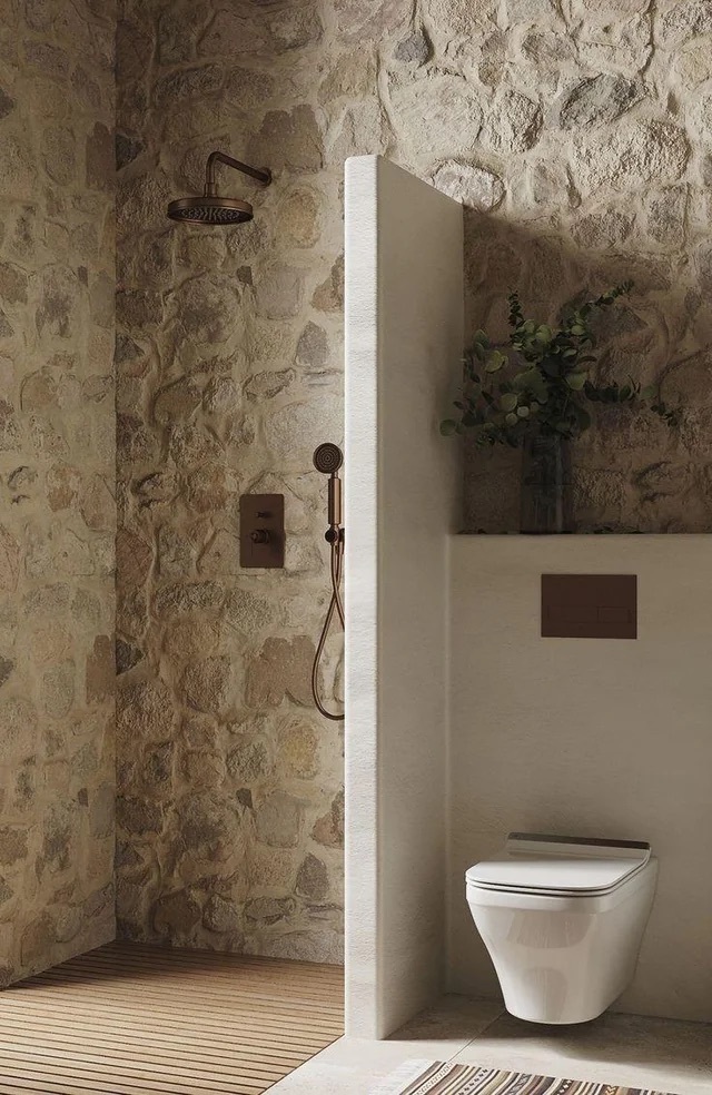 Modern rustic bathroom: stone shower walls, bronze fixtures, and wall-mounted toilet.