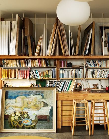 Artist studio interior with custom wooden bookshelves, painting storage, and modern globe lighting.
