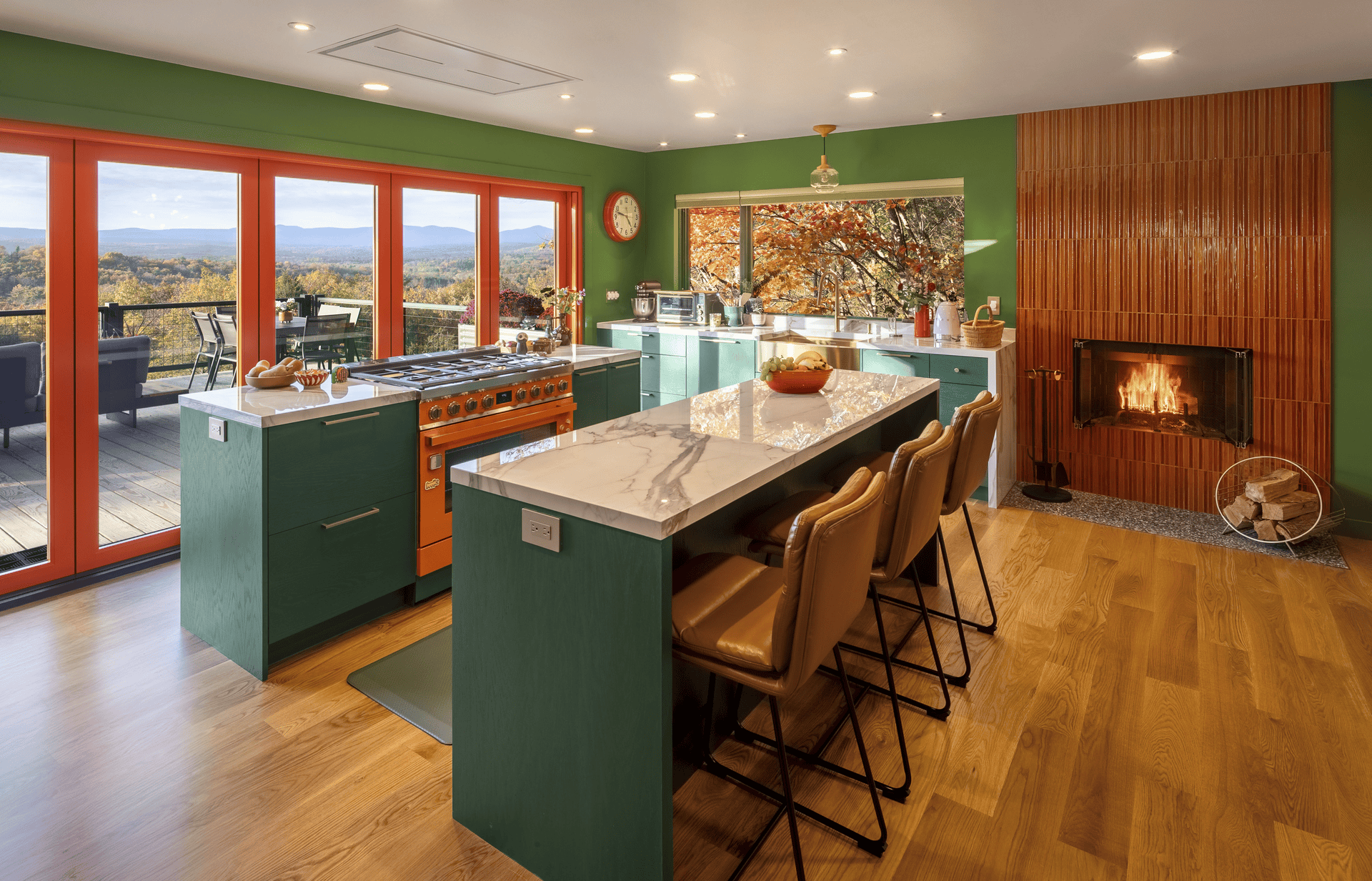 A perspective of the kitchen with the bifold doors wide open, showcasing an unobstructed view of the rolling mountains. The natural light highlights the contrast between the green walls, the marble island, and the warmth of the wood floors.