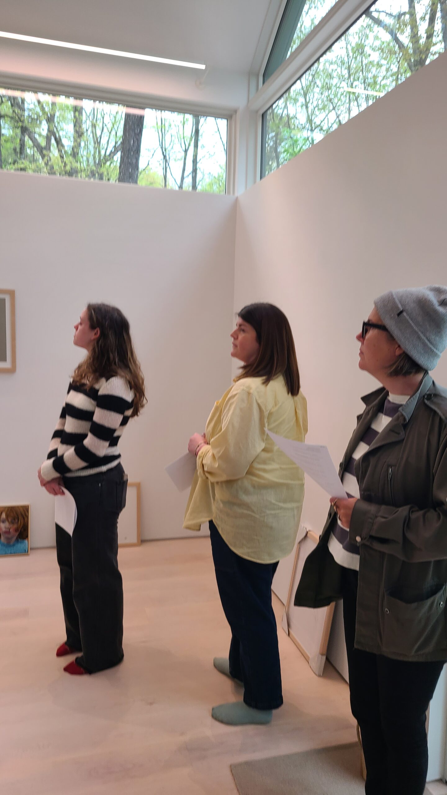 Three women standing in a bright, modern art gallery, looking up at minimalist artwork on white walls.