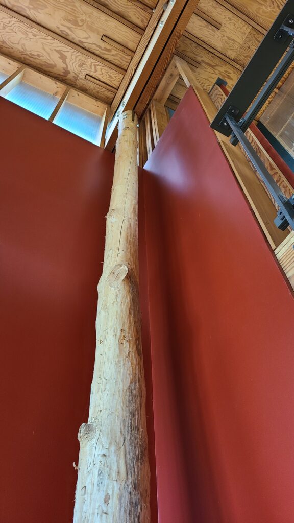A wide upward view of a tall, natural log post supporting a modern ceiling between two vibrant red walls.