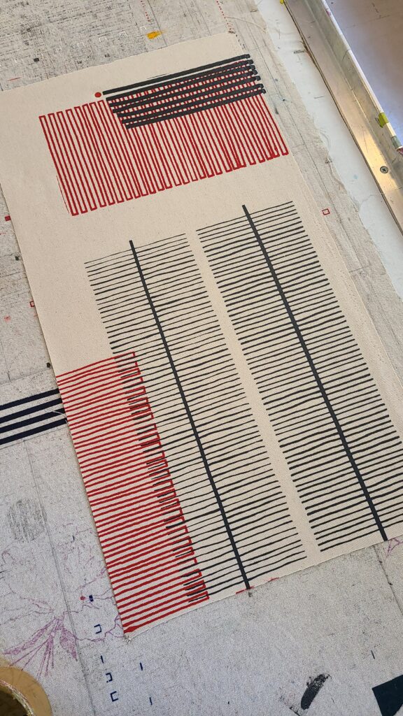 A close-up of a fabric sample featuring a modern abstract print of thin black and red horizontal lines.