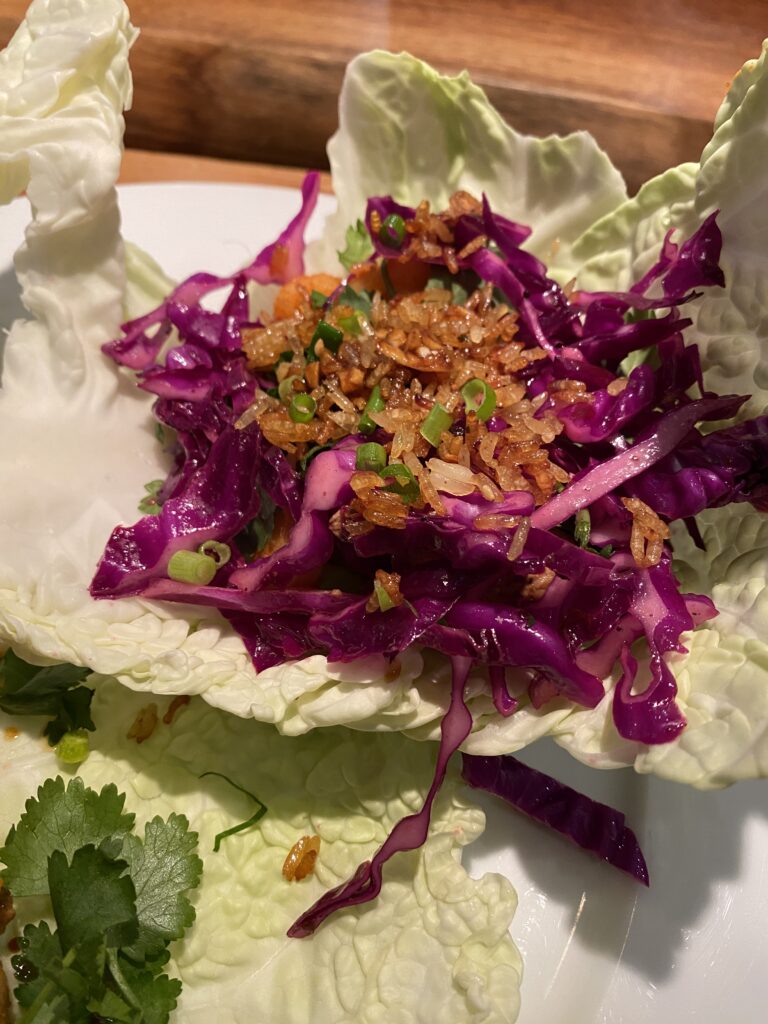 A colorful food dish featuring bright purple cabbage and toasted grains served inside a large, crisp light-green lettuce leaf.