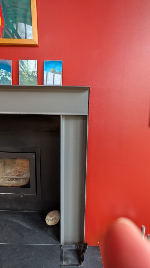 A modern grey fireplace mantel set against a vibrant red wall, featuring small landscape photos and a decorative stone.