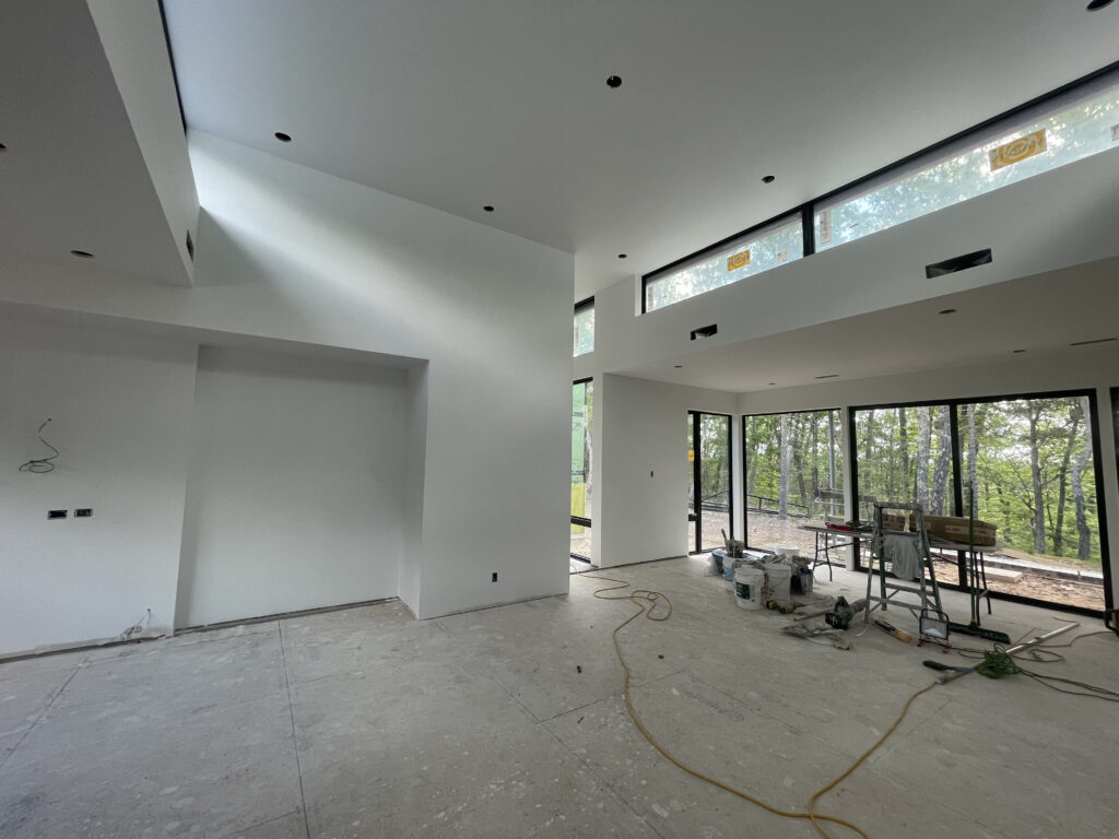 Interior construction progress at Quattro showing freshly primed walls and ceilings, with siding work visible through windows.