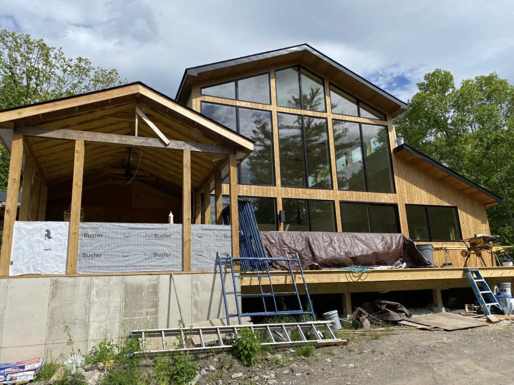 Exterior siding installation nearly complete at Pond Lane, with the home's profile and materiality taking shape against the landscape.