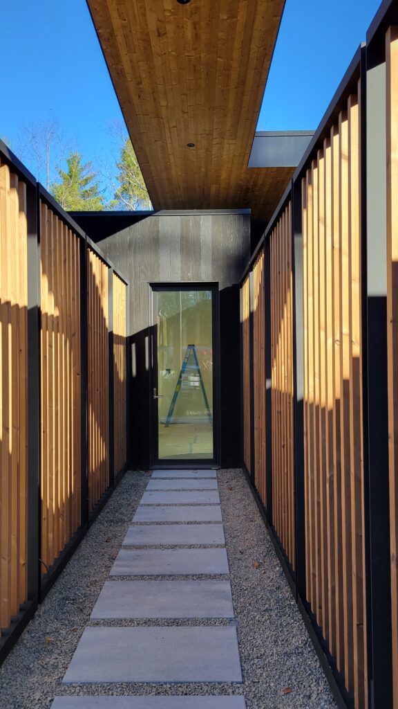 Walkway flanked by cedar batten screen walls leading to a glass entry door at Fermata