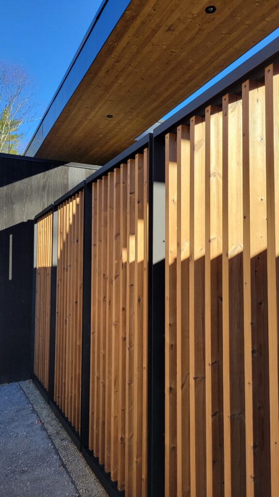 Angled view of a sunlit cedar batten screen wall beneath a wood soffit at Fermata