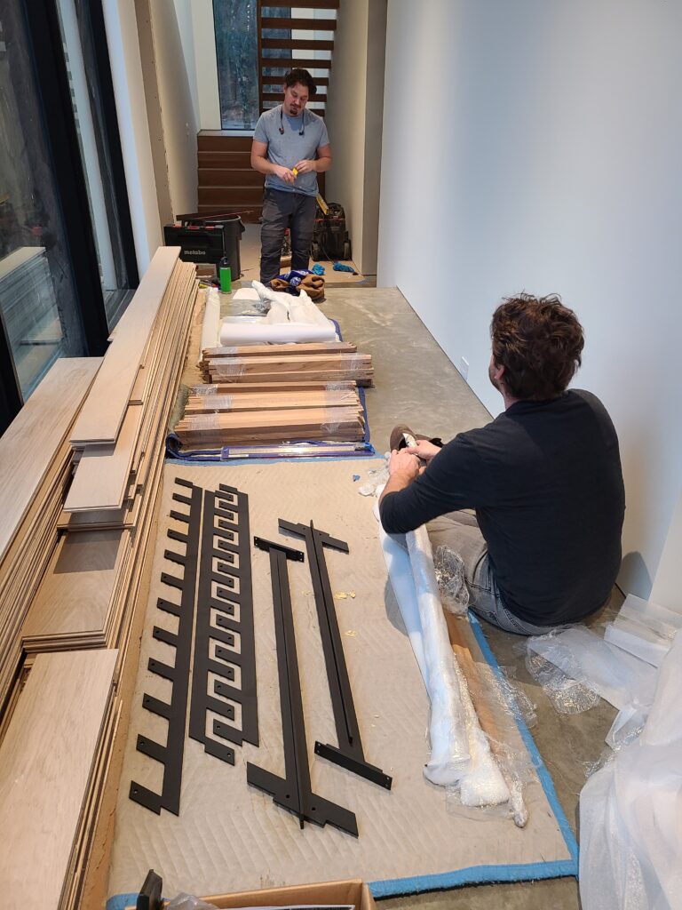 Craftsmen assembling white oak stair treads and blackened steel baluster brackets on site