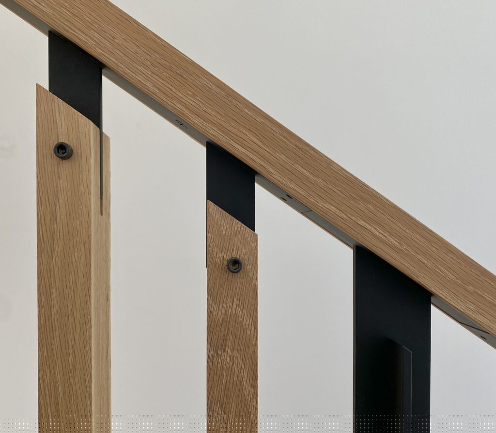 Finished white oak handrail with slender black steel balusters and exposed hex screws