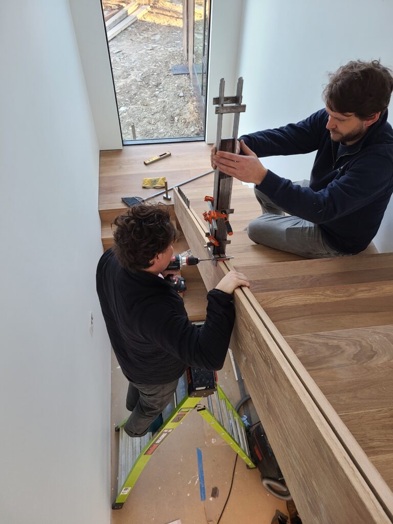 Two installers clamping and aligning a solid oak handrail with an internal steel support core
