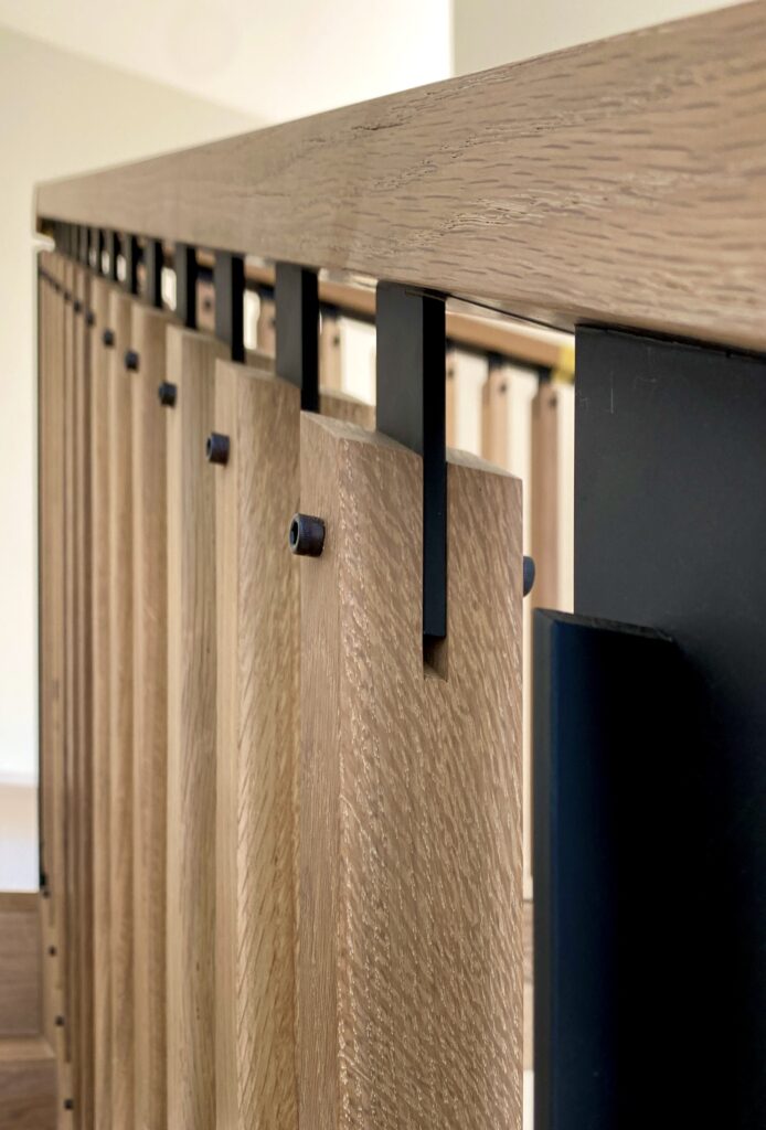 Close-up of a modern oak stair railing with repeating black steel flat-bar balusters