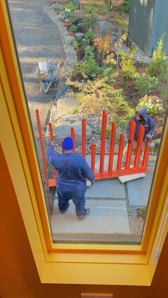 Overhead view of installers positioning the orange steel fence posts beside a stone-lined garden bed