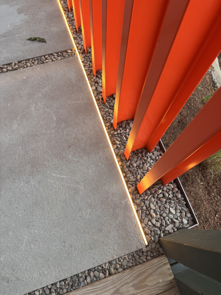 Close-up of the orange steel fence base with integrated LED strip lighting along a stone walkway