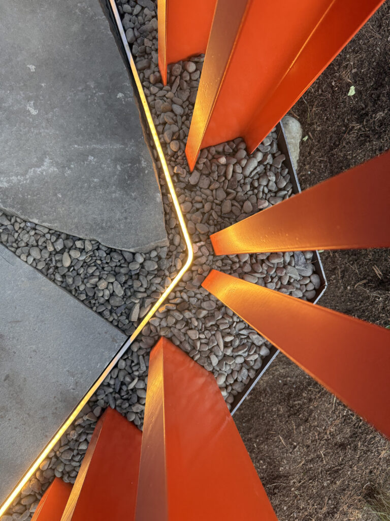 Overhead detail of orange steel fence posts fanning outward from a corner with glowing LED edge lighting