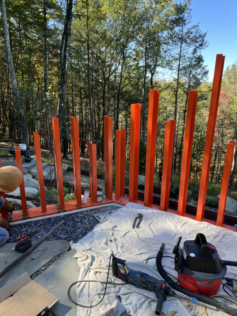 Freshly installed orange steel fence posts against a wooded Hudson Valley backdrop