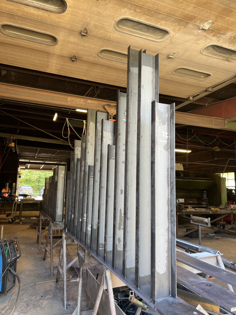 Row of graduated-height steel fence posts lined up in a fabrication shop before finishing