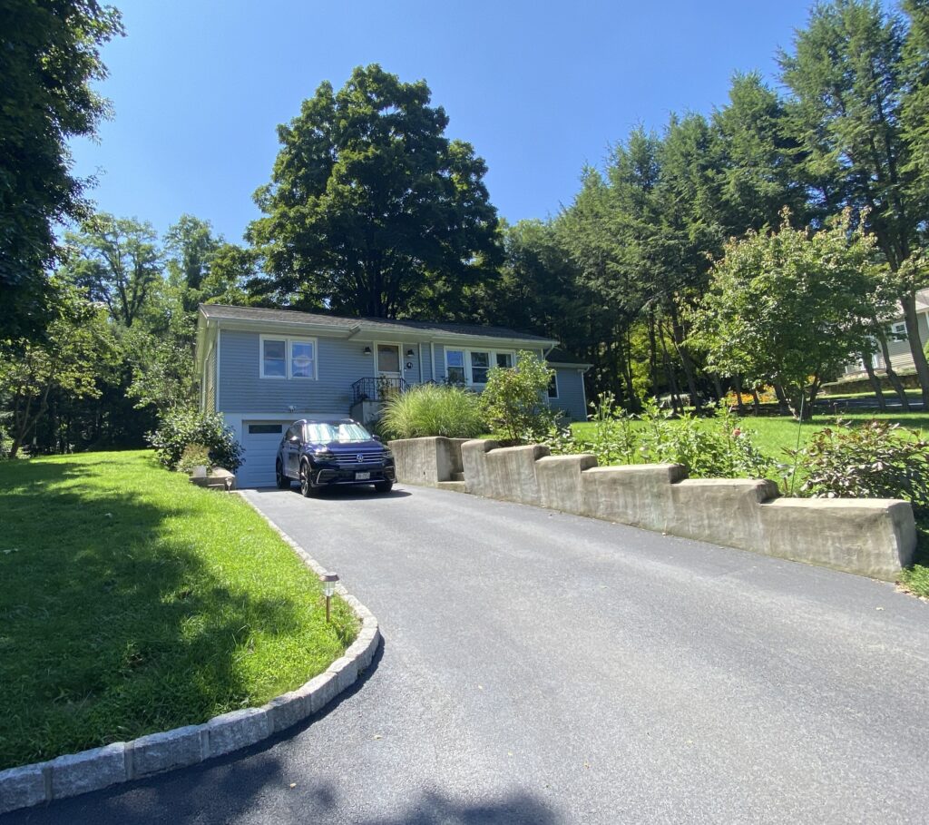 Sunny image of an existing home and driveway, with blue light blue siding and double hung windows.