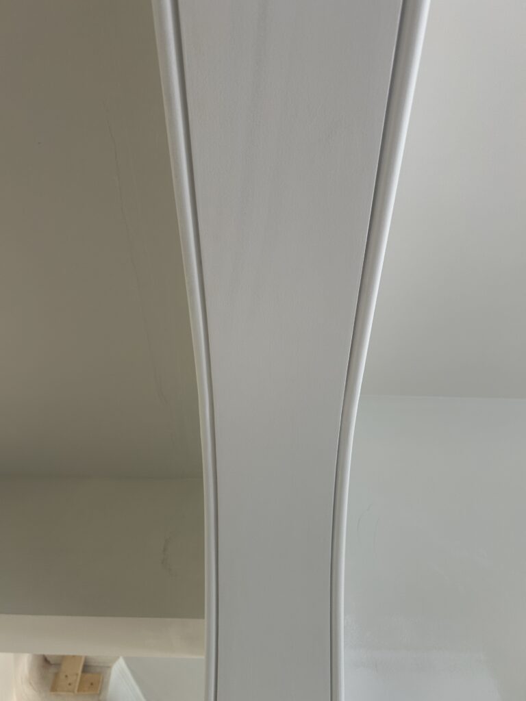 Close-up of a white curved architectural trim detail with visible seam lines against matching walls