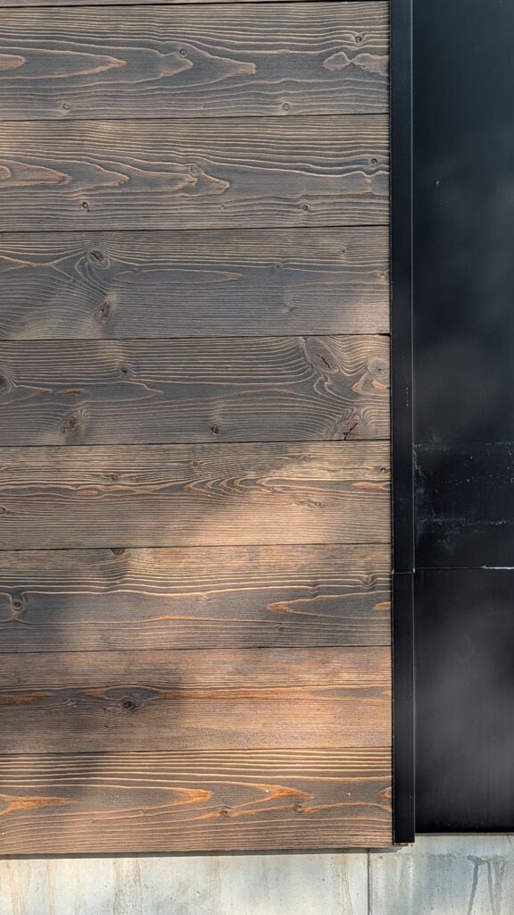 Close-up of dark stained horizontal wood siding meeting a black metal gutter on a building exterior