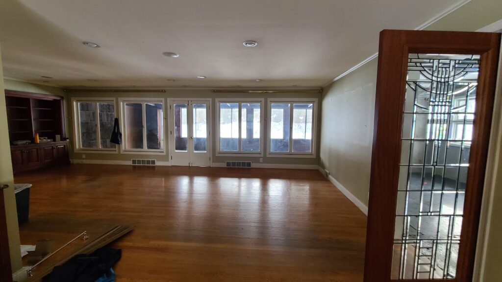 Empty living room with hardwood floors, a row of frosted multi-pane windows, a dark wood built-in bookshelf, and a leaded-glass door frame