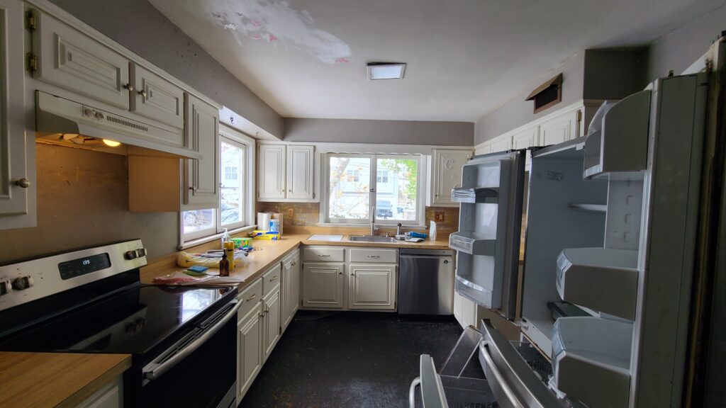 Dated kitchen mid-renovation prep with white cabinetry, black electric range, laminate countertops, and an open refrigerator