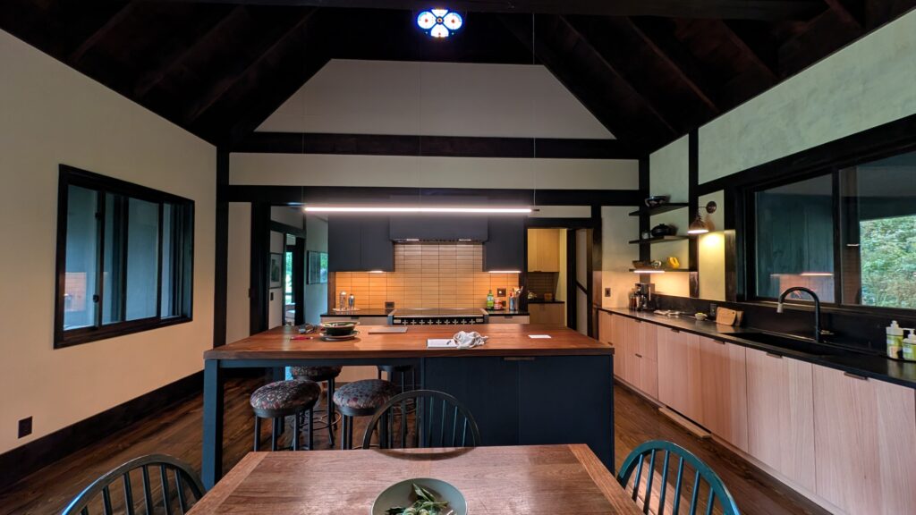 Finished dining and kitchen area with dark wood beamed ceiling, a round stained-glass ceiling fixture, and a linear pendant over the island