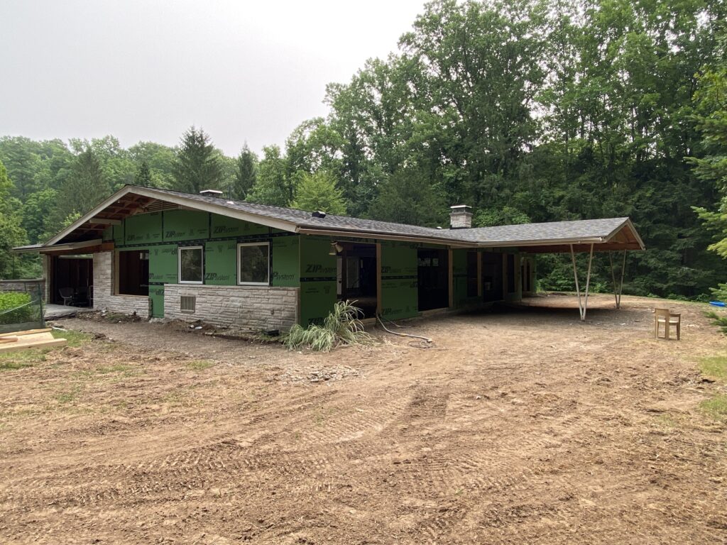 Exterior of a mid-construction single-story home with green ZIP System sheathing, partial stone veneer, and a covered outdoor sitting area