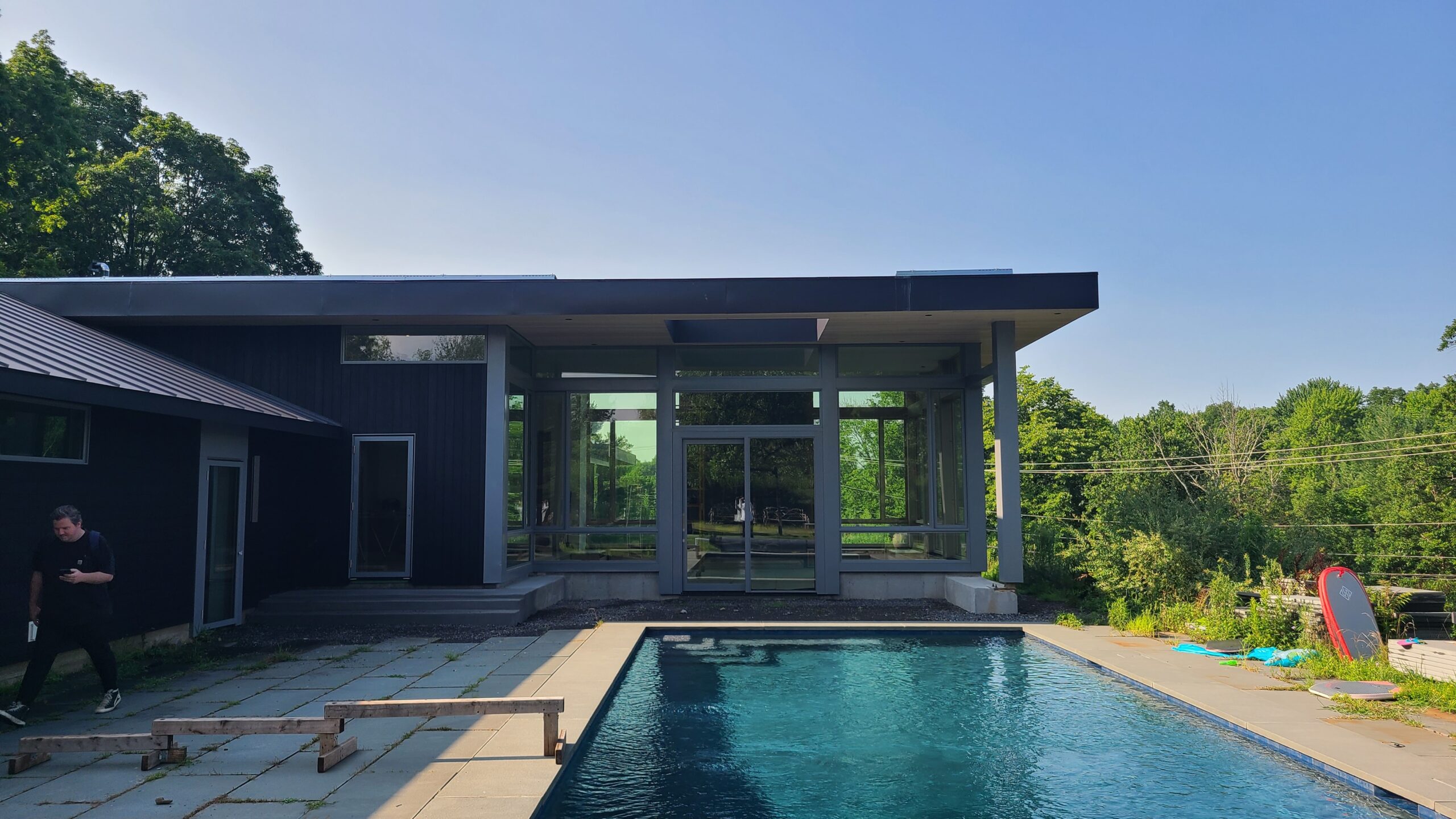 Exterior of a modern black house from the pool side, showing large glass walls, a covered patio, and a rectangular pool