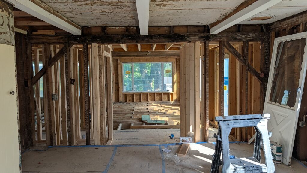 Interior of an older home under renovation showing a mix of exposed original hand-hewn ceiling beams and new dimensional lumber framing