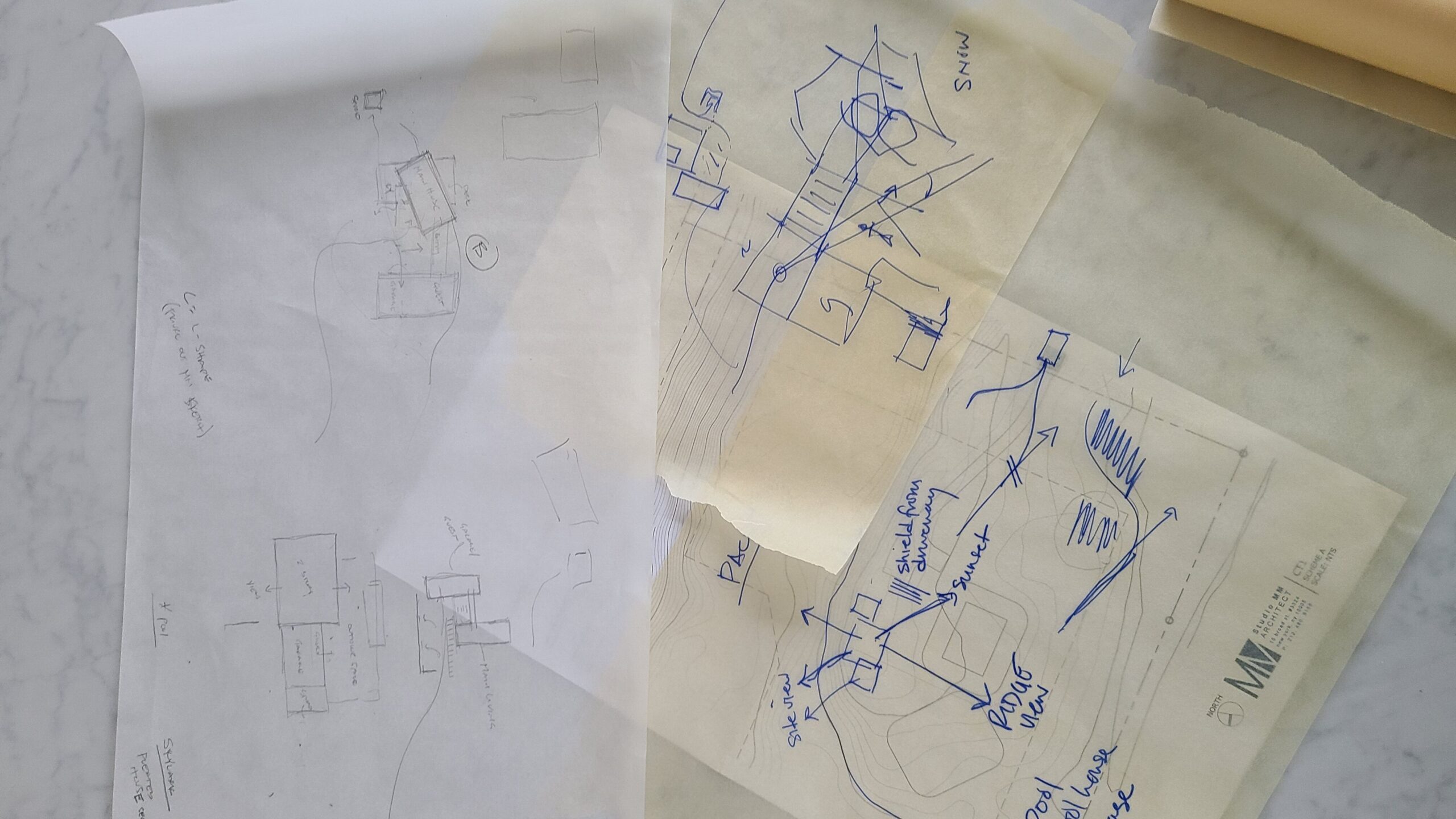 Overlapping hand-drawn sketches on trace paper and a printed site plan with blue pen notes on site view, sunset, ridge view, pool, and pool house