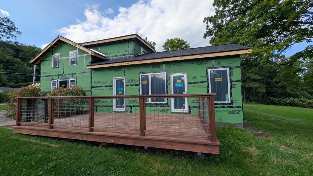 Exterior of a two-story home mid-construction wrapped in green ZIP System sheathing with white-trimmed Marvin and Infinity windows and a new deck