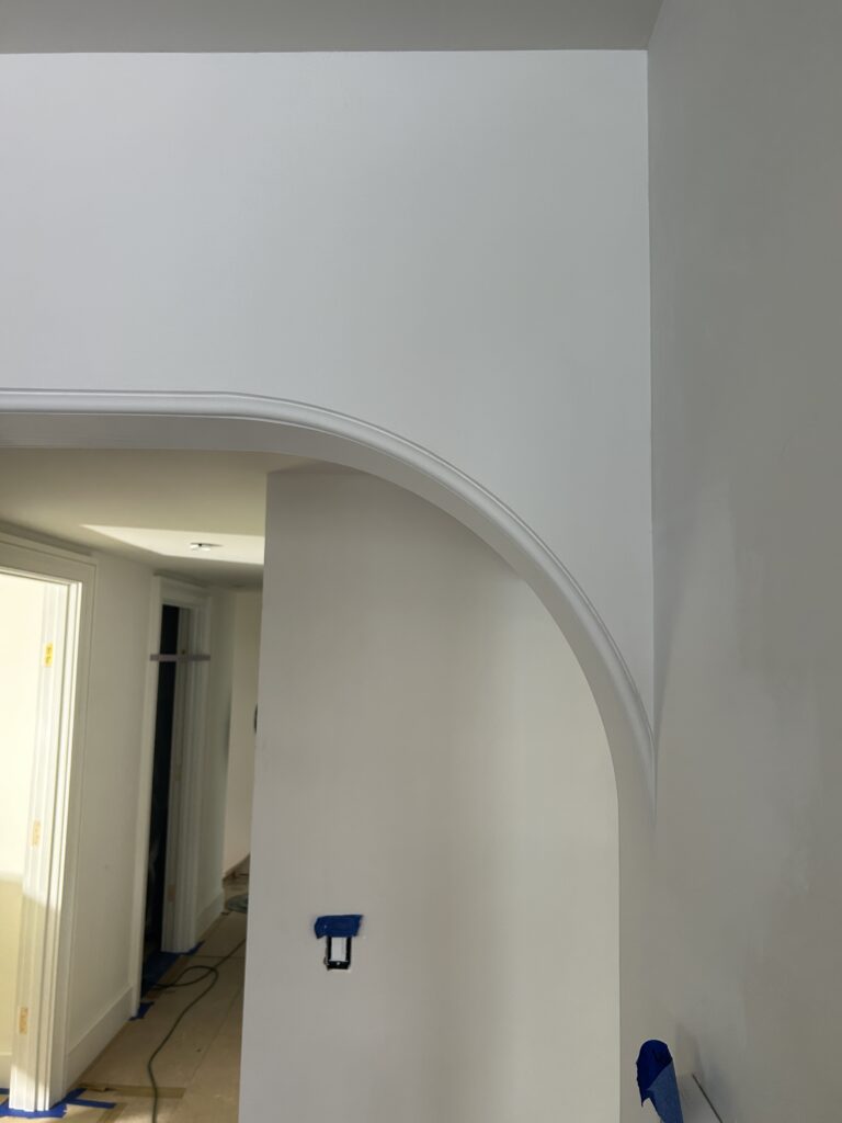 Interior view of an unfinished white archway opening between rooms, with visible outlet box and blue painter's tape
