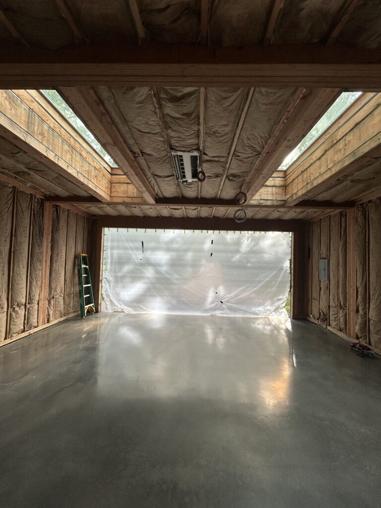 Interior of an unfinished garage or studio space with exposed wood framing, insulation, two skylights, and a mini-split unit
