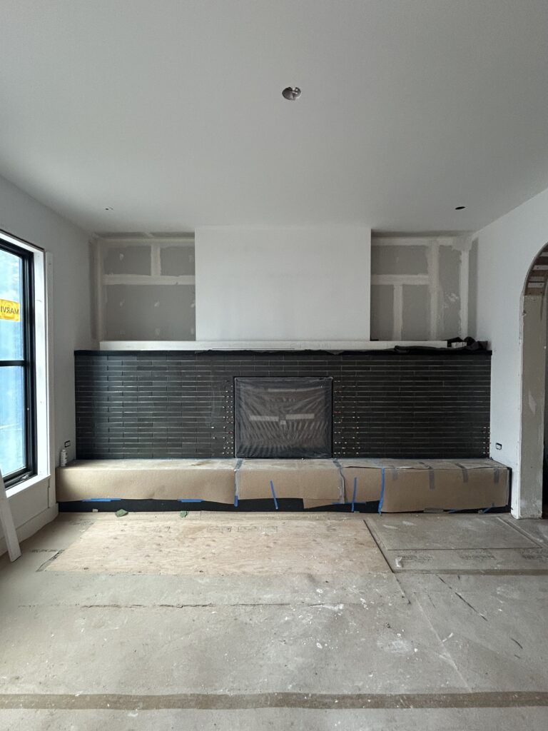 Unfinished living room with a black brick-tile fireplace surround, protected stone hearth, drywall in progress, and a subfloor